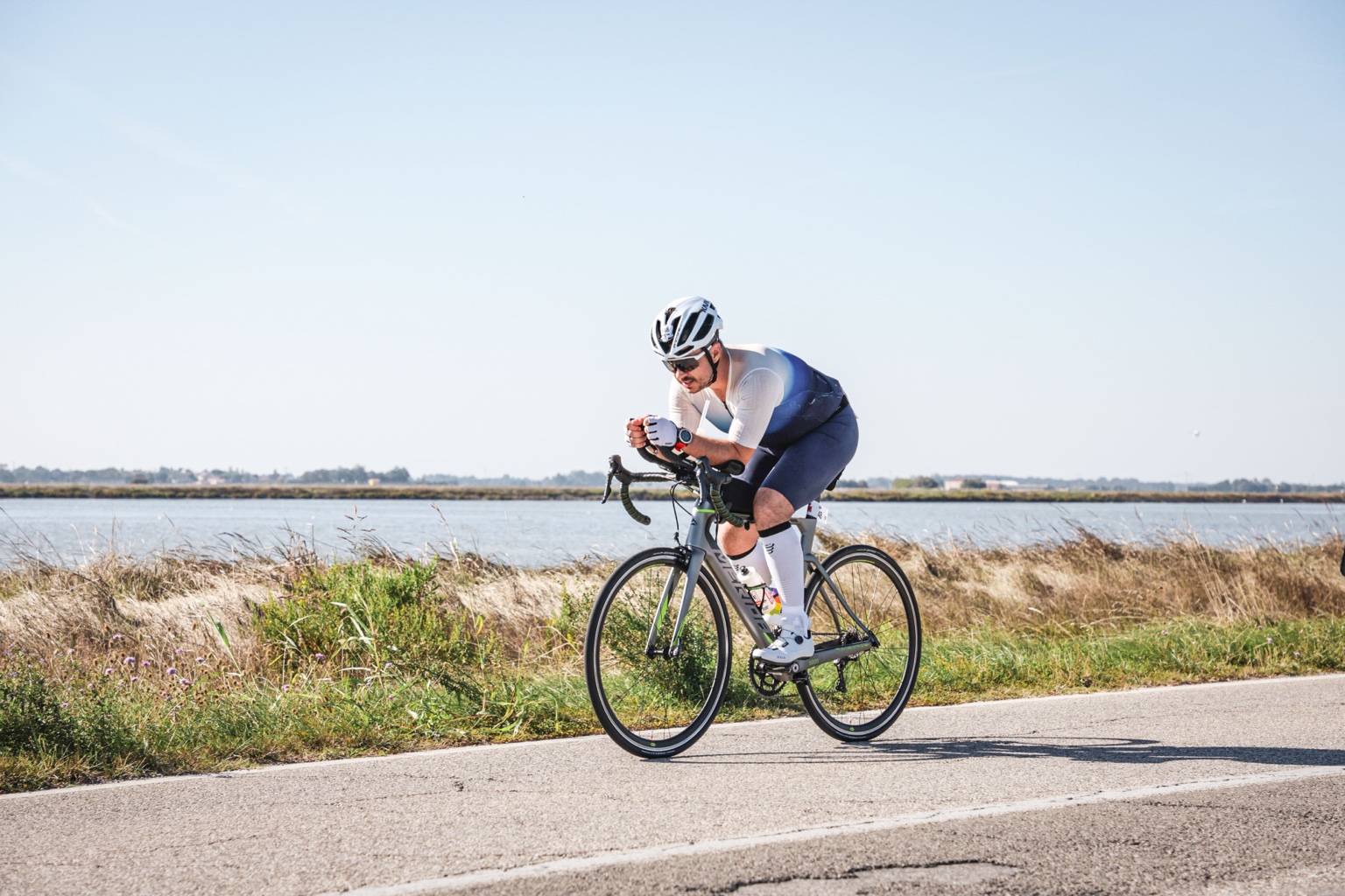Damian na rowerze w pozycji aerodynamicznej, na drodze obok wody.